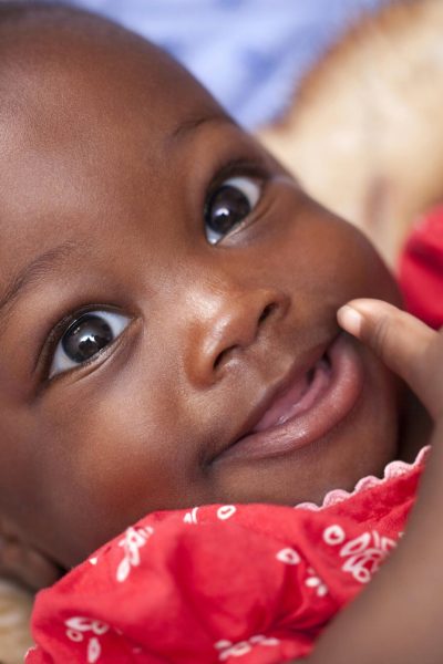 Close-up portrait of a happy baby smiling in a bright red outfit, showcasing joy and innocence.